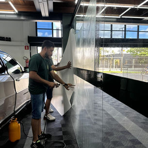 Profissionais da Art Finesse manuseando PPF transparente para aplicação meticulosa em carro esportivo.