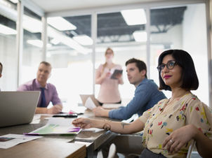 אישה יושבת בשולחן עם אנשים נוספים, משוחחים ומבלים יחד באווירה חברתית.