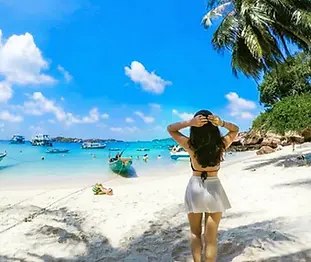 Tourist standing on a white sand beach, admiring the turquoise bay with traditional wooden fishing boats in the Southern Islands of Phu Quoc.