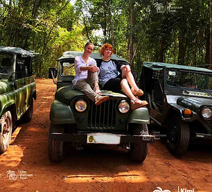 Three classic military jeeps lined up on a jungle track with happy travelers sitting on th