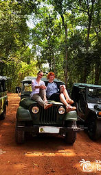Three classic military jeeps lined up on a jungle track with happy travelers sitting on th