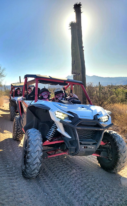 Travelers enjoying a desert ATV tour driving a Honda UTV next to a gian saguaro cactus
