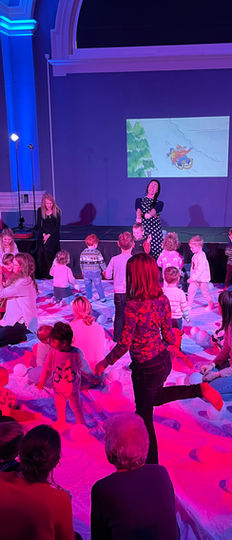 A busy storytelling show with engaged, interactive families, grown ups and kids playing. Special lighting, music and sound with illustrations projected create a magical theatrical space.