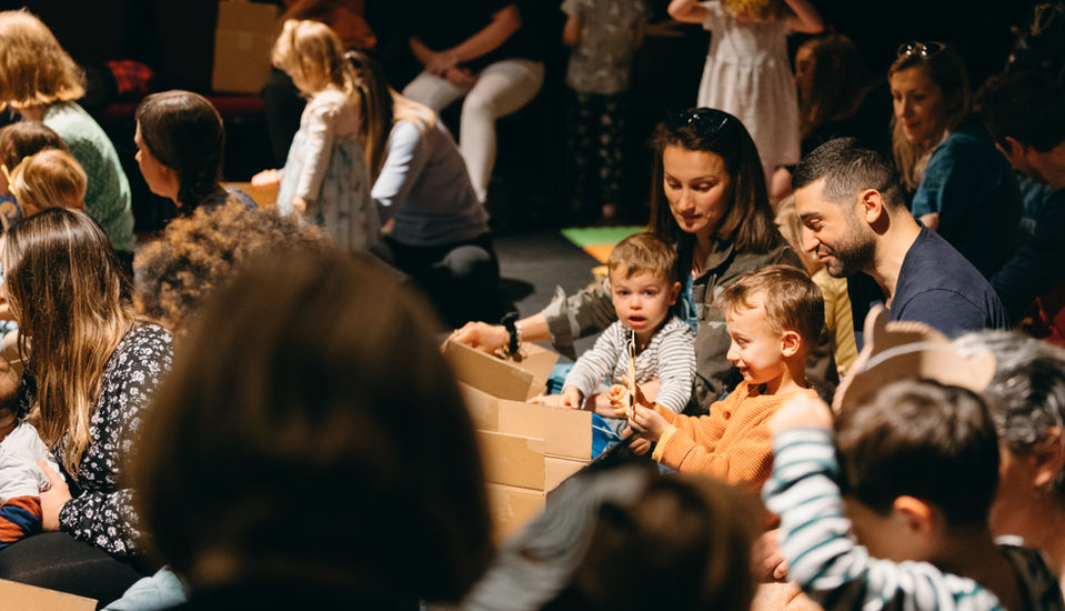 An audience view of familes, grown ups and their children opening the storytelling prop box