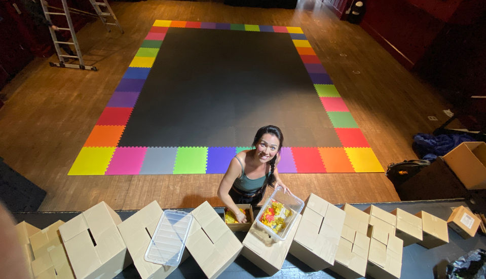 A view from the stage at the Astor in Deal. Hannah filling storytelling prop boxes used throughout the show with interactive props. The black and colourful matting is set up in the background for storytelling play and for Hannah to perform on