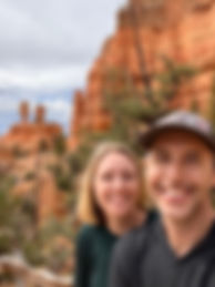 A smiling couple takes a selfie in front of red rock formations and Pinon Pine trees near our Bryce Canyon National Park vacation rental in Kanab, Utah.