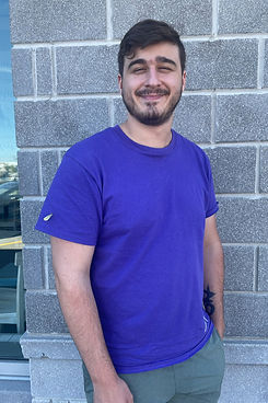 A Young Man In A Purple Shirt And Green Shorts Posing In Front Of A Brick Wall Smiling