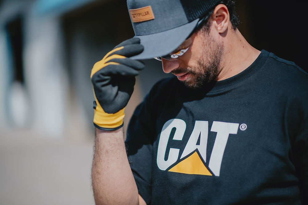 Man wearing premium workwear: CAT t-shirt, cap, and gloves