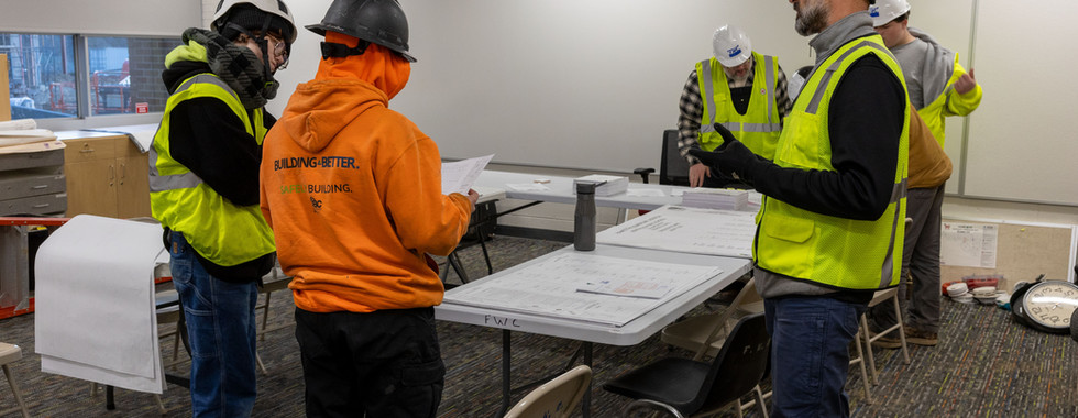 Instructor guiding students through construction drawings on active job site