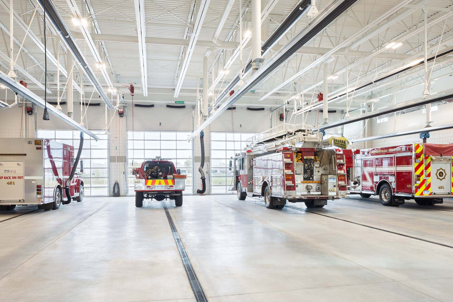 Spacious fire station apparatus bay with polished concrete floors, overhead doors, and multiple emergency vehicles parked inside a newly constructed facility