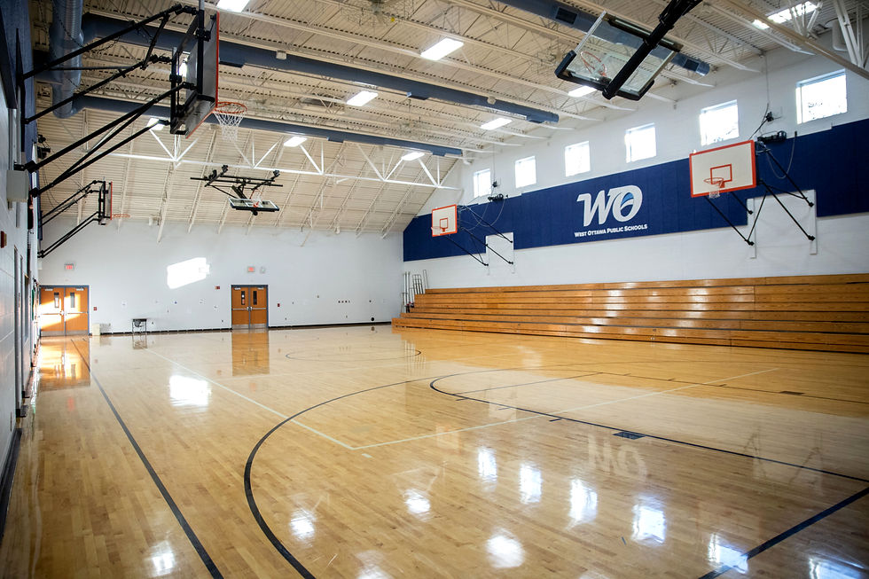 Finished school gymnasium with hardwood court, bleachers, and basketball hoops, showcasing completed K-12 construction project