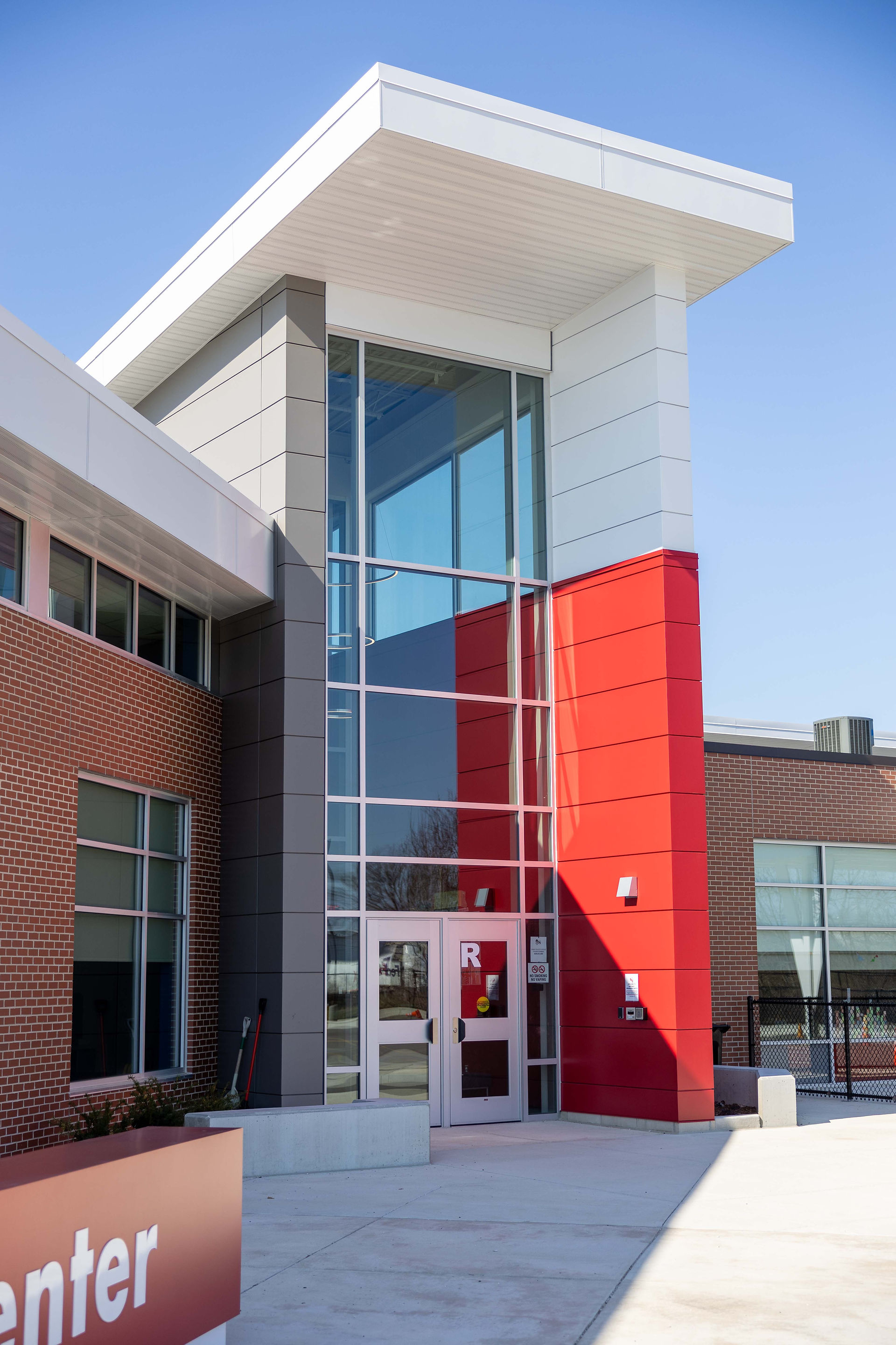 Contemporary school entrance tower with glass curtain wall and red accent paneling