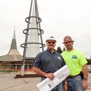 Two men standing near a modern outdoor sculpture.
