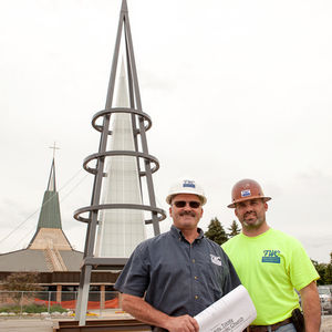 Two men standing near a modern outdoor sculpture.