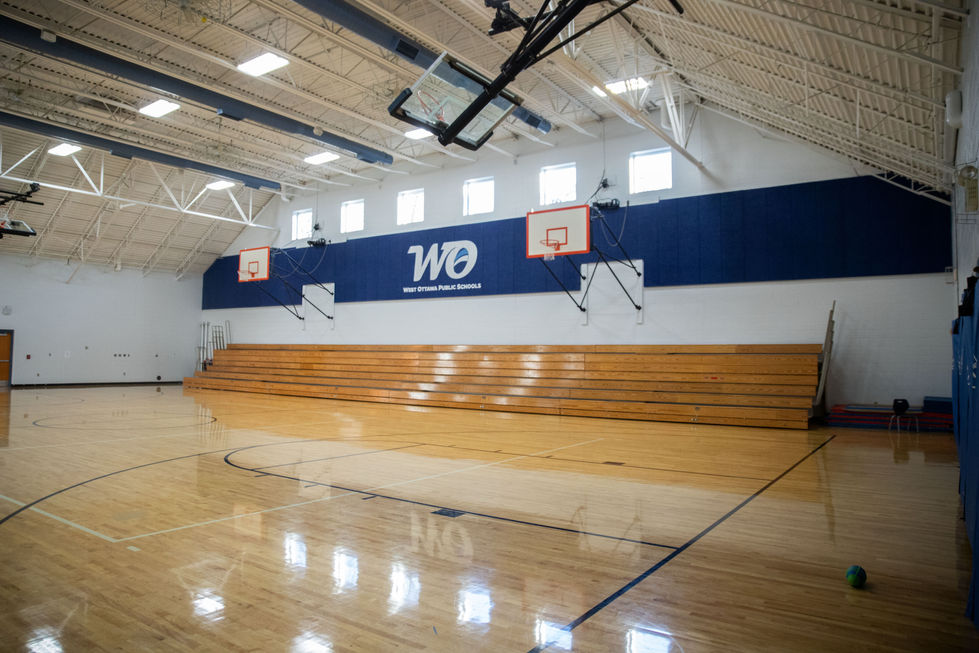 Empty gymnasium with wooden bleachers and basketball hoops.