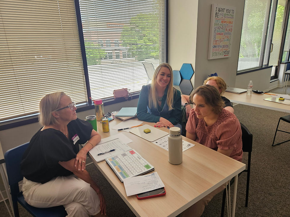 Four women sit around a table in a bright classroom.