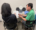 Two people in a classroom, one points to a whiteboard labeled Affirmative while the other listens; the workshop participant is asking for consent before supporting the learner's communication practice.