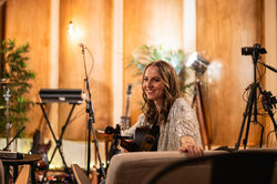 Rachel Makena holding her acoustic guitar while relaxing on a settee