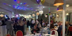 People drinking at the bar and sitting at tables in a hotel function room at the 262 Charity Ball