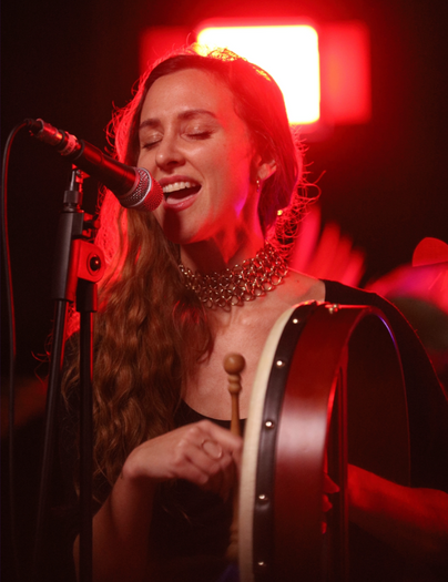 Woman in joyful pleasure practice, singing and playing a bodhrán drum under red light without shame or performance