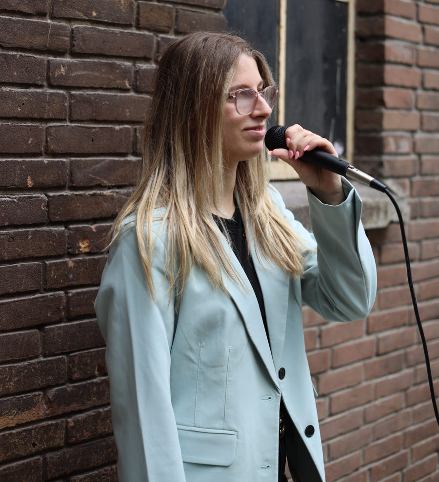 Isabella Sotera zingt in een microfoon voor een bakstenen muur