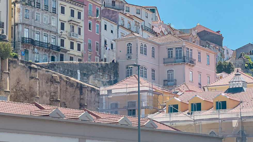 Layered view across Coimbra, with rooftops and buildings climbing the hillside beneath a pale sky.