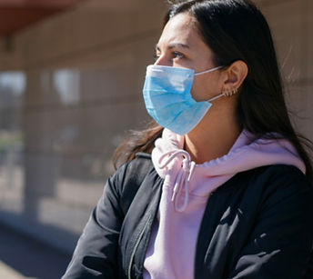 Person outside of a building wearing a medical mask with arms crossed