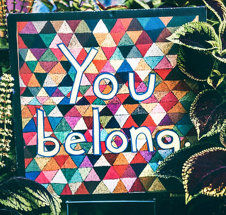 Multicolor triangles in a quilt with white letters stating "You belong"