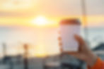 Hand holding a coffee cup against a vibrant sunrise over a the Manzanita Beach waterfront. Warm hues create a serene and peaceful mood.