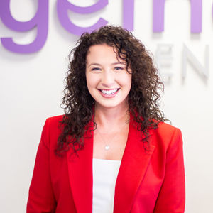 Headshot of female dentist in a red blazer, curly brown hair smiling.