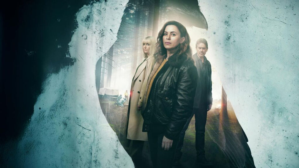 Eve Myles, Katherine Kelly, and Dougray Scott stand in a forest clearing, seen through the silhouette of a bird on frosted glass. The woman in front wears a dark jacket, with a man and another woman in lighter clothes behind her.
