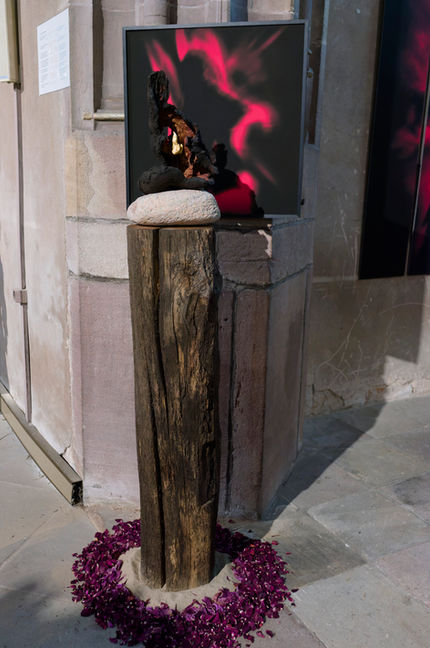 La poutre de chêne a servi de charpente dans une ferme.
Elle symbolise la lignée dans laquelle s'inscrit l'individu.
Au pied de l'installation, des pétales de rose rouge et de pivoine pourpre. En Alsace, la pivoine est appelée "rose de Pentecôte". Le pourpre est la couleur de la laine filée par Marie au Temple de Jérusalem lorsqu'elle a été préparée par l'Esprit de Pentecôte.