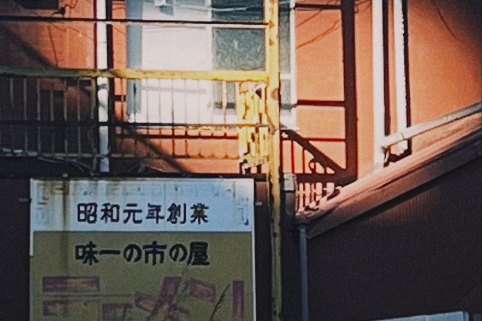 Red building with yellow railing in sunlight, featuring a Japanese sign with black text. The mood is warm and nostalgic.