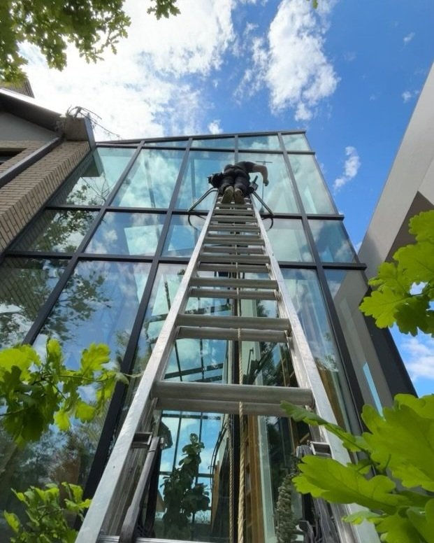Man on a large ladder cleaning a wall of windows