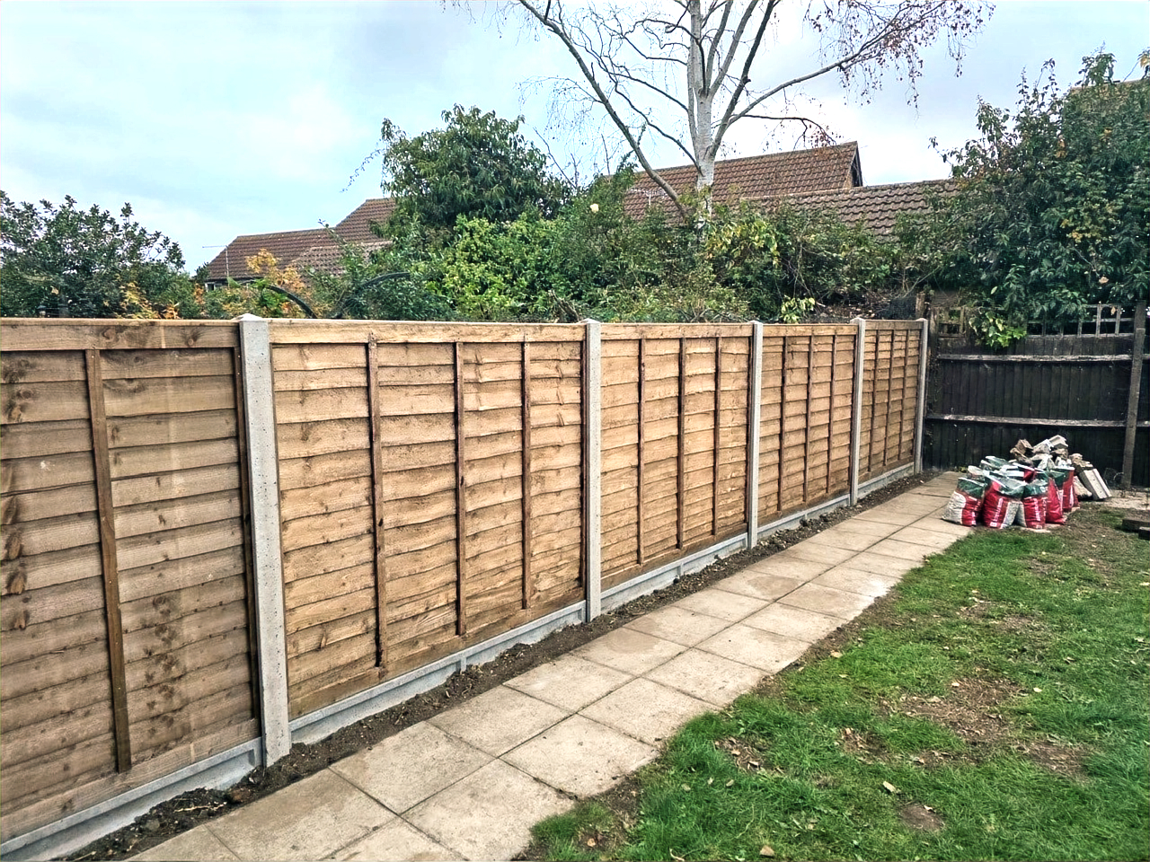 Timber garden fencing with concrete posts alongside a paved path