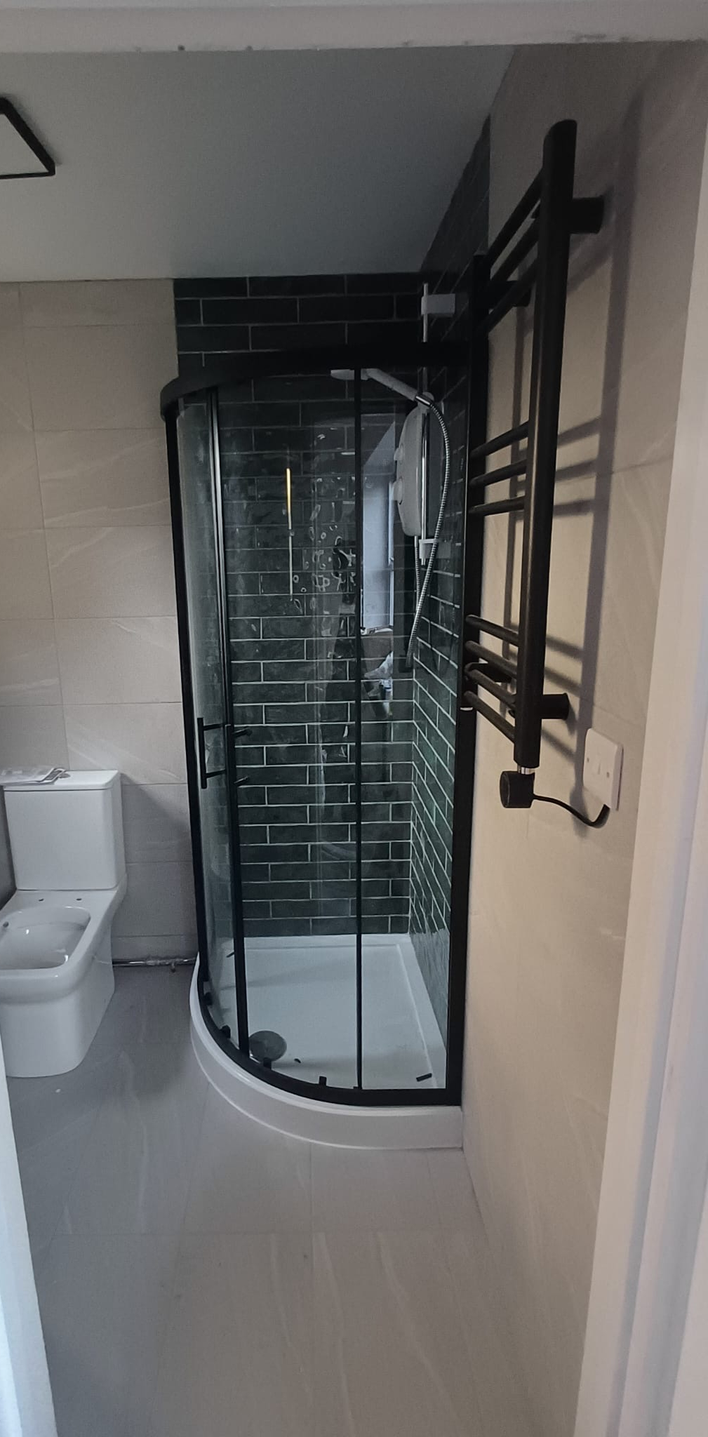 Bathroom with a curved shower enclosure, dark tiles and a heated towel rail