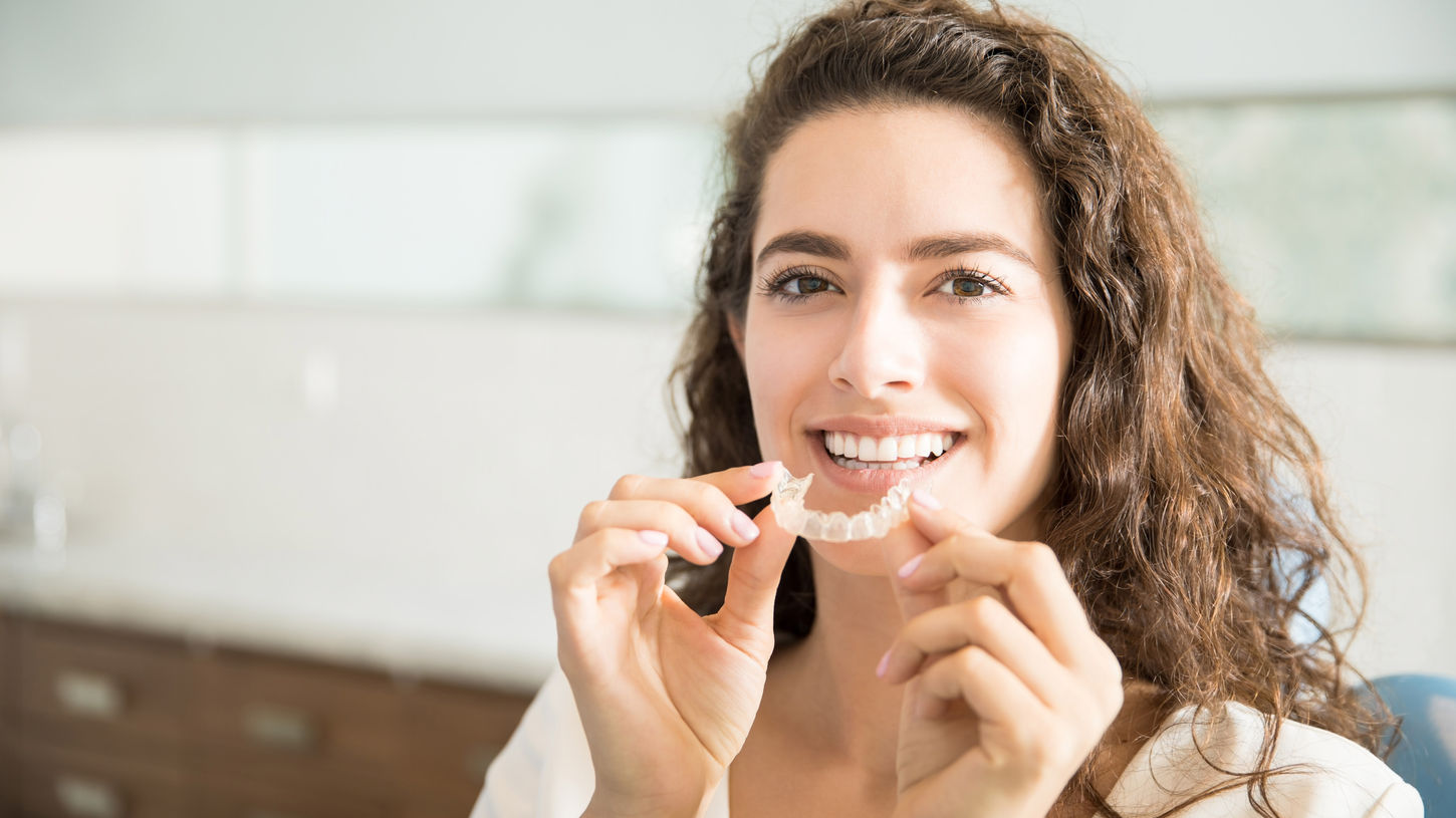 Woman smiling while holding her clear aligner or retainer