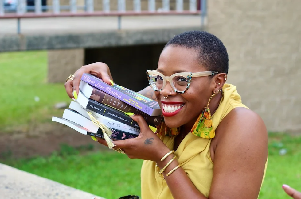 Black woman with low cut hair and glasses smiling holding a stack of books