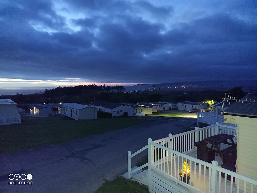 Serene evening view from caravan decking, overlooking the tranquil landscape of Brynowen, Borth with the glow of distant lights and a colorful horizon in Aberystwyth, Mid Wales.