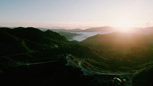 Sunrise over lush green mountains and winding roads, with misty valleys and a serene sky, creating a peaceful and tranquil scene.