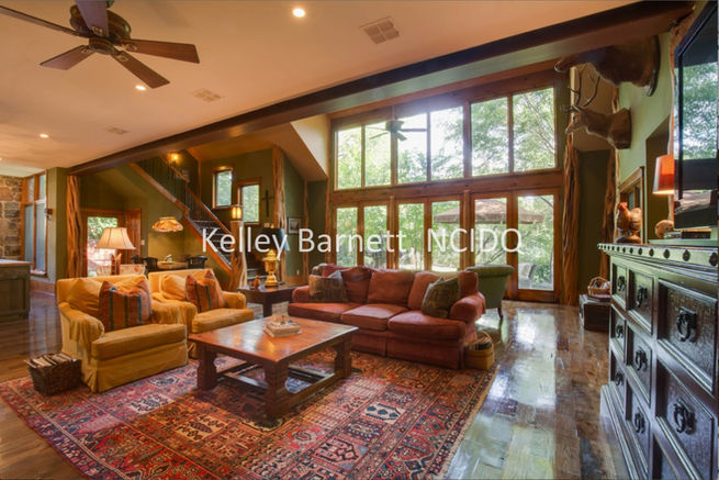 Warm green walls and solid wood plank floors envelope 2 story window walls, embossed leather entertainment center, antique Persian rug, iron beam ceiling support, cypress tree trunk supports, and Western belt buckle ceiling fan