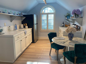 LVT floors, blue walls, kitchenette, teal tufted chairs, marble top dining table, white shaker cabinets, stainless shelving, LED track lights.