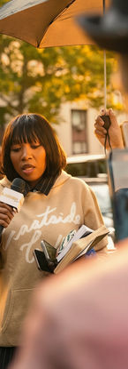 Reporter speaking into a microphone on a city street. Photography by Rafael Mercedes.