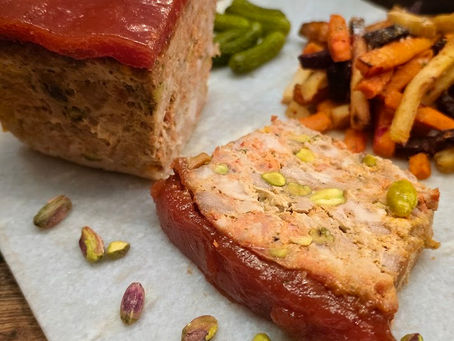 Sliced pistachio-studded meat terrine with glossy red glaze, pickles and fries on parchment paper.