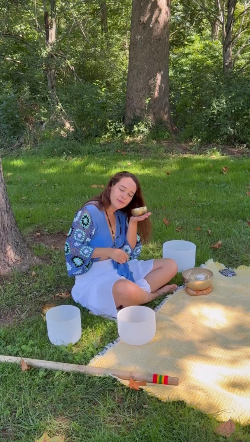 A woman sitting on the grass listening to a Tibetan singing bowl.