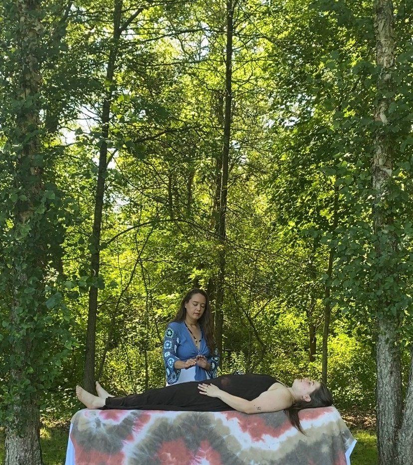 A woman performing Reiki on her client who is laying on a table, in nature