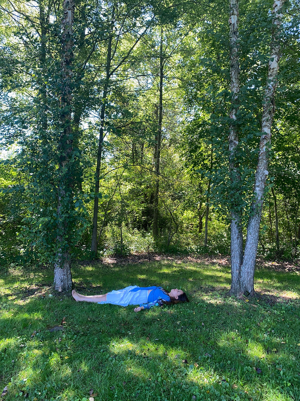 A woman laying on the grass between trees with a long white skirt and blue blouse
