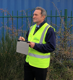 SWL Security Vulture CCTV man in hi vis with ipad completing a site survey in front of container and perimeter.
