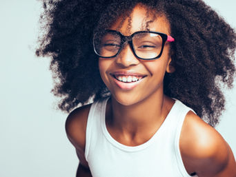 A teen girl with a big smile is wearing big glasses with thick frames.