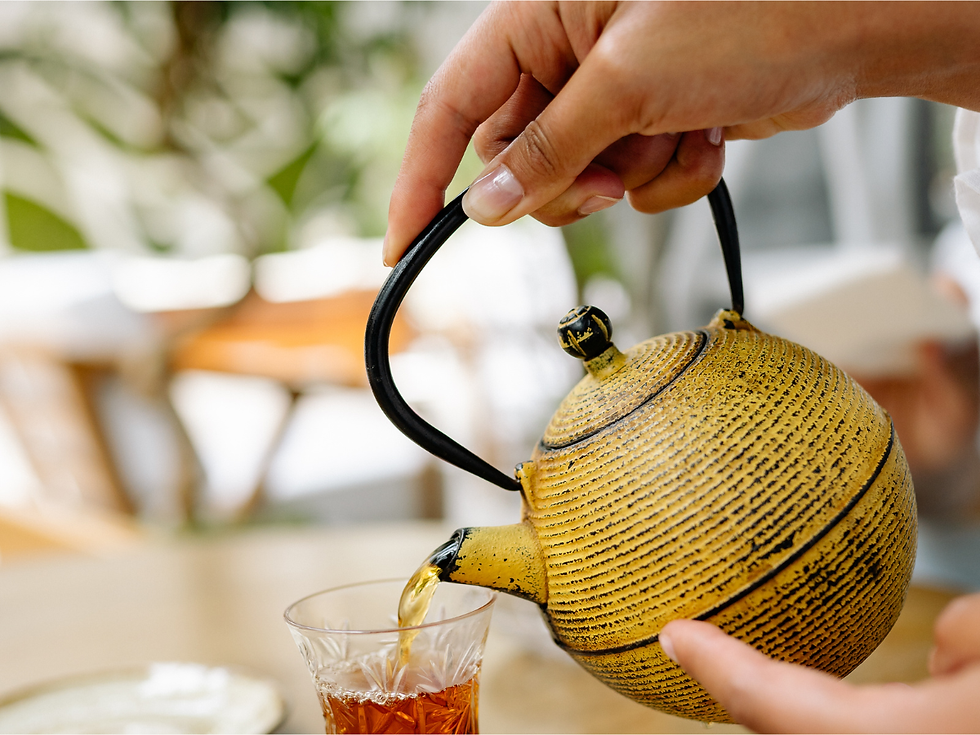 Hand holding a yellow tea kettle pouring tea into a glass cup.